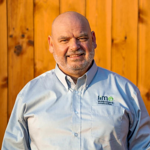 Man wearing a light blue shirt with a logo in front of a wooden fence