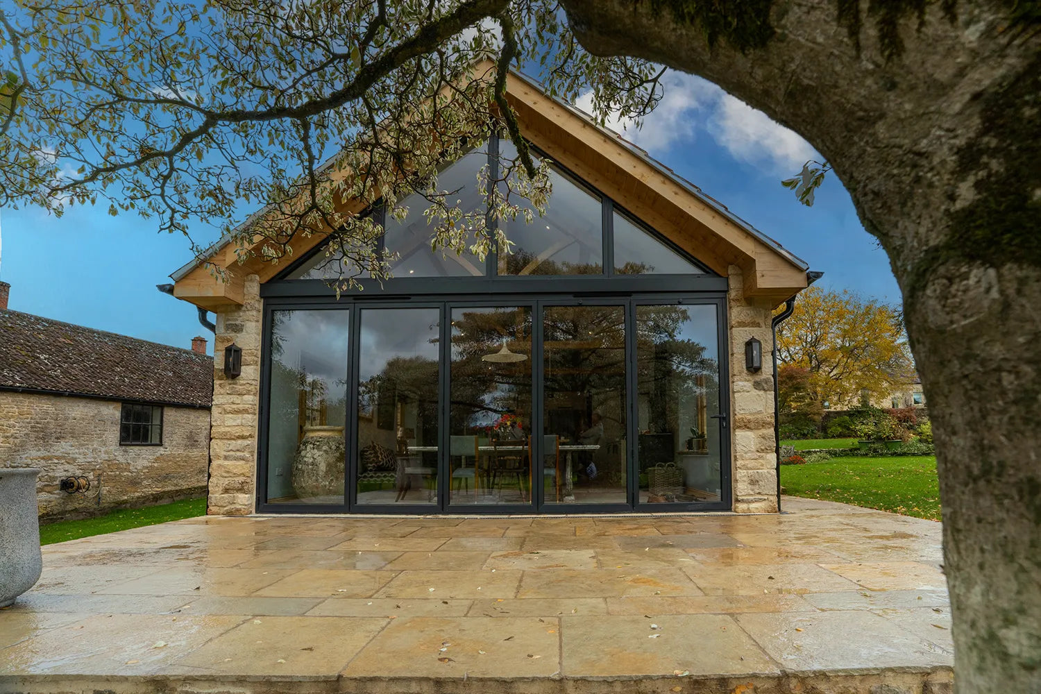 Modern house extension with large glass windows and stone exterior, surrounded by trees and greenery.